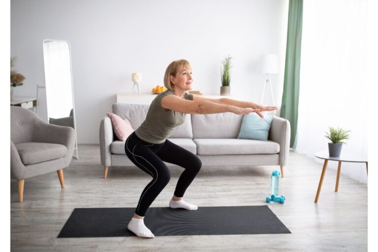 Active mature lady doing squats on yoga mat indoors